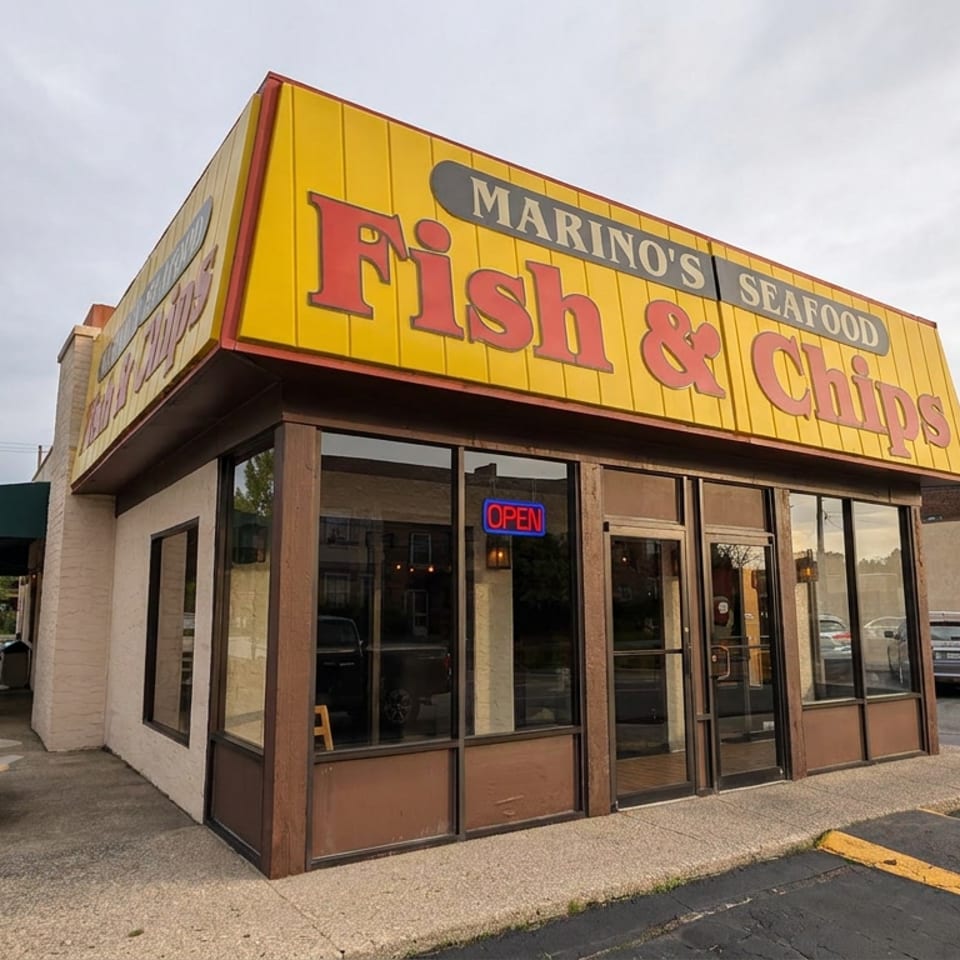 Exterior of Marino's Seafood Fish & Chips restaurant with outdoor picnic tables, neon open sign, and entrance sign.