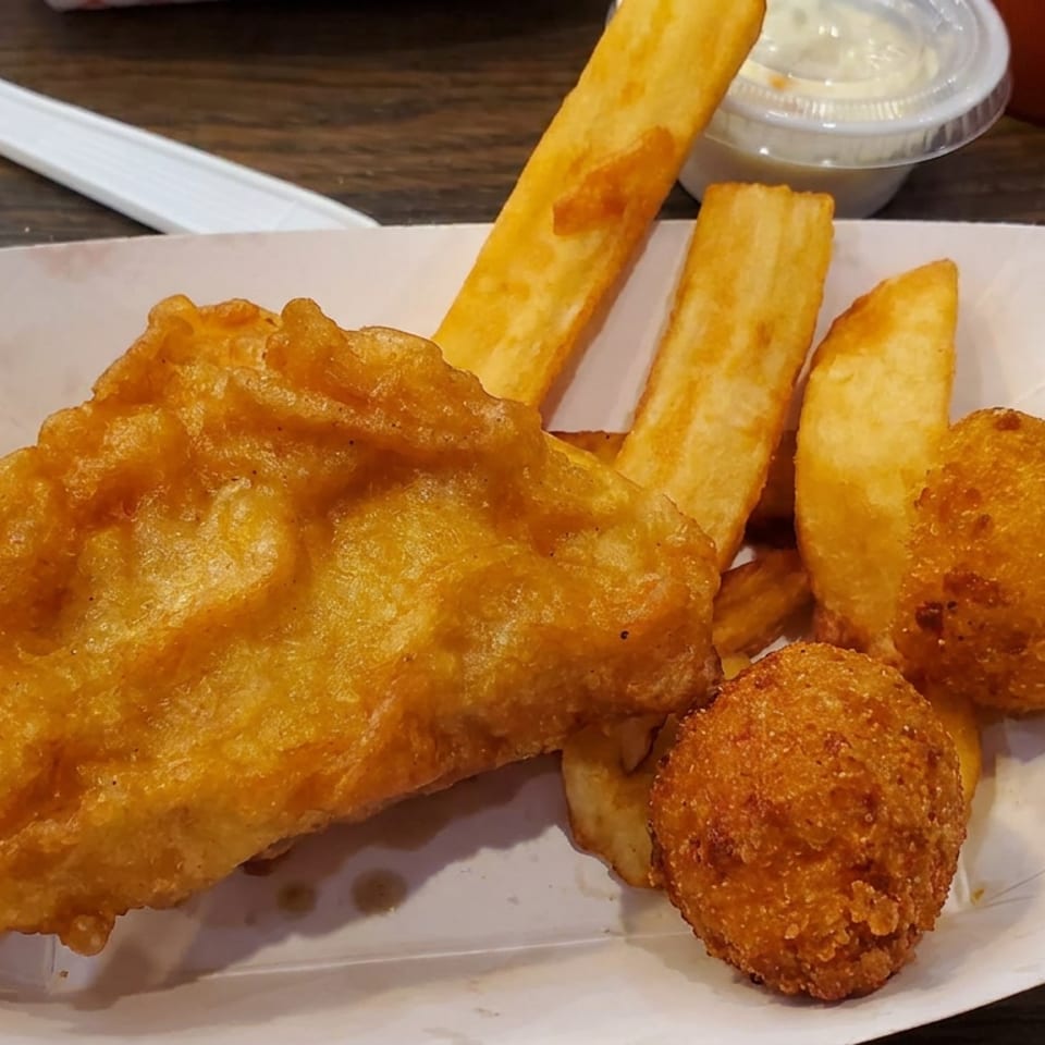 Golden battered fish with thick fries and two crispy hush puppies served on paper-lined tray.