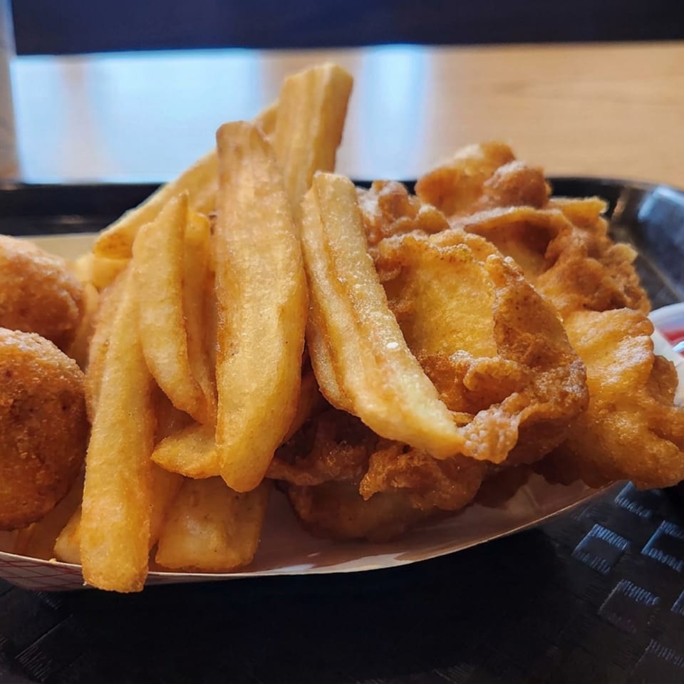 Basket of golden fried fish, chips, hush puppies, and onion rings served with ketchup and tartar sauce.