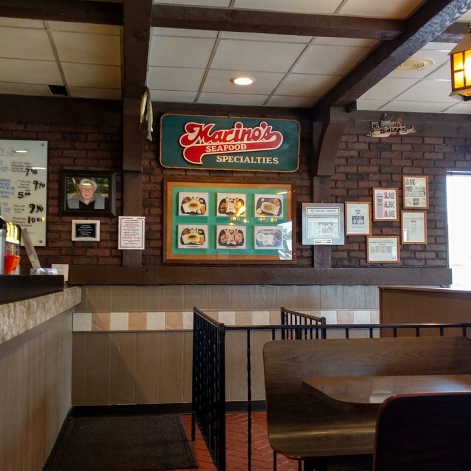 Warmly lit seafood restaurant interior with lanterns, wooden booths, brick walls, framed memorabilia, and Marino’s Seafood specialties sign.